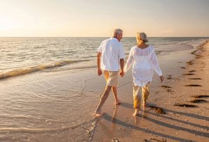 Retired elderly couple walking on the beach at sunset